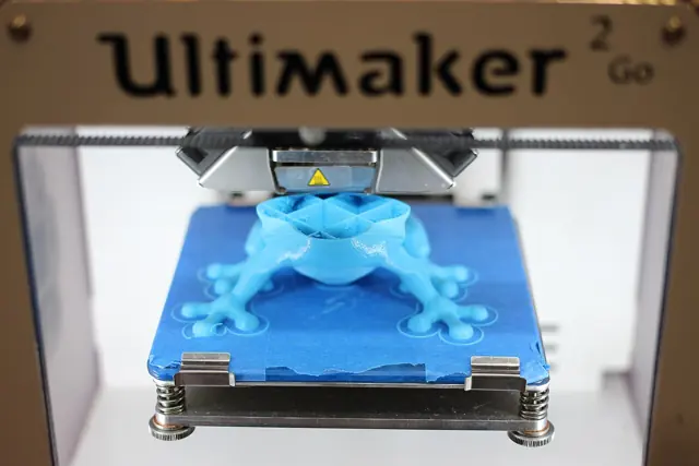 Impresora 3D de filamento imprimiendo una pieza azul sobre la cama de impresión